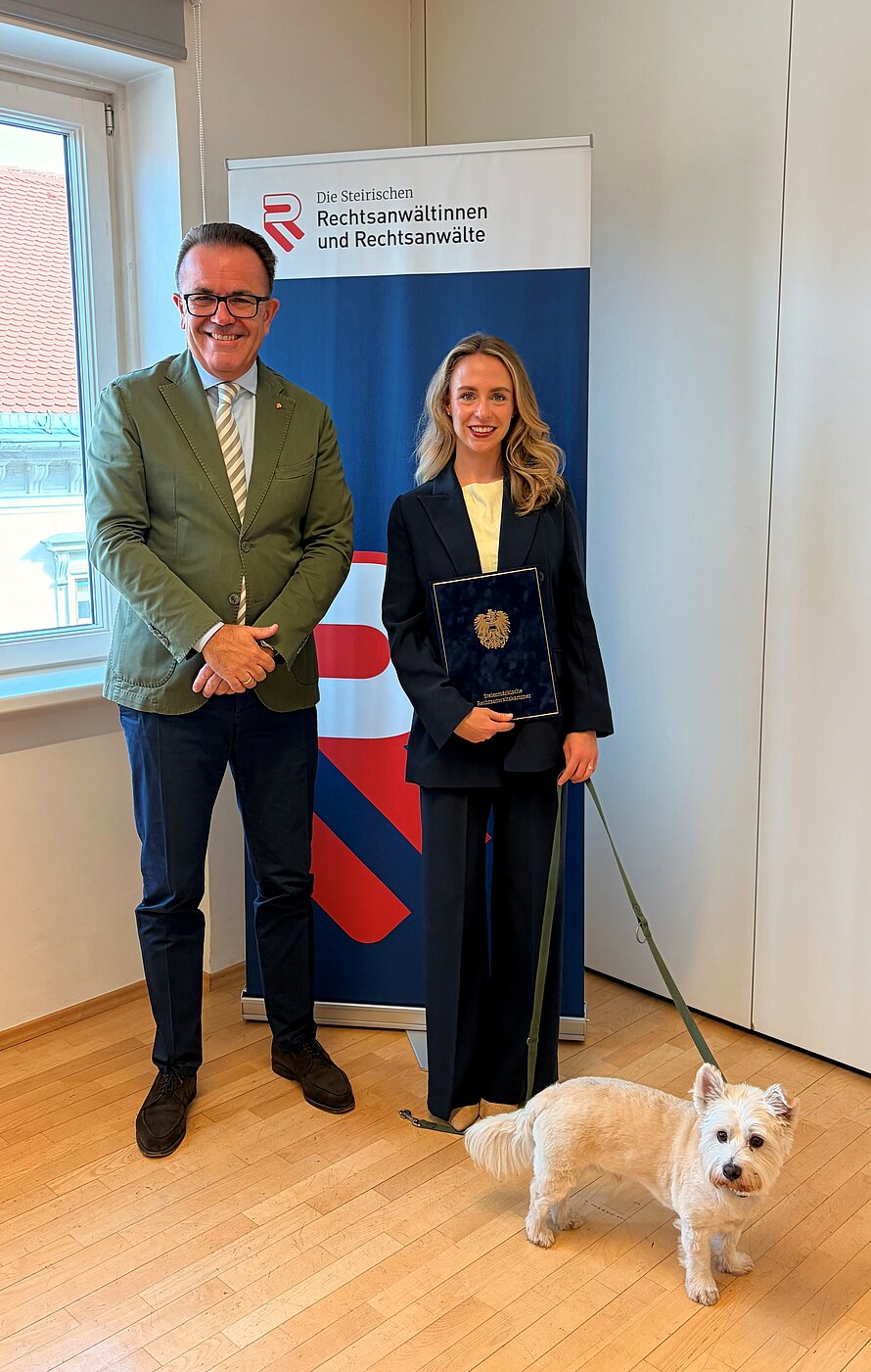 Präsident Kropiunig mit der frisch angelobten Rechtsanwältin, die einen Hund an der Leine führt.